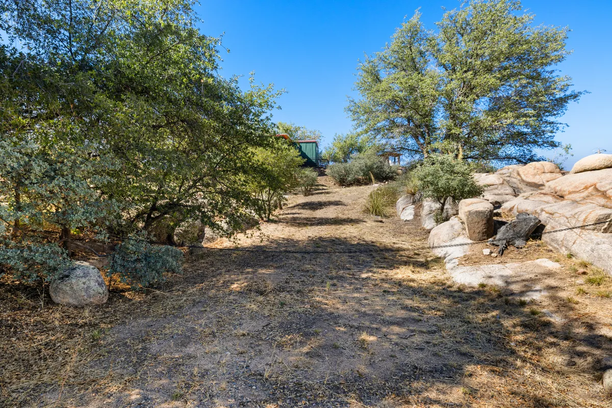 A serene exterior pathway lined with trees and dramatic rock formations, showcasing the immediate natural context just beyond the home. The pathway evokes the spirit of adventure and easy access to the surrounding landscape.