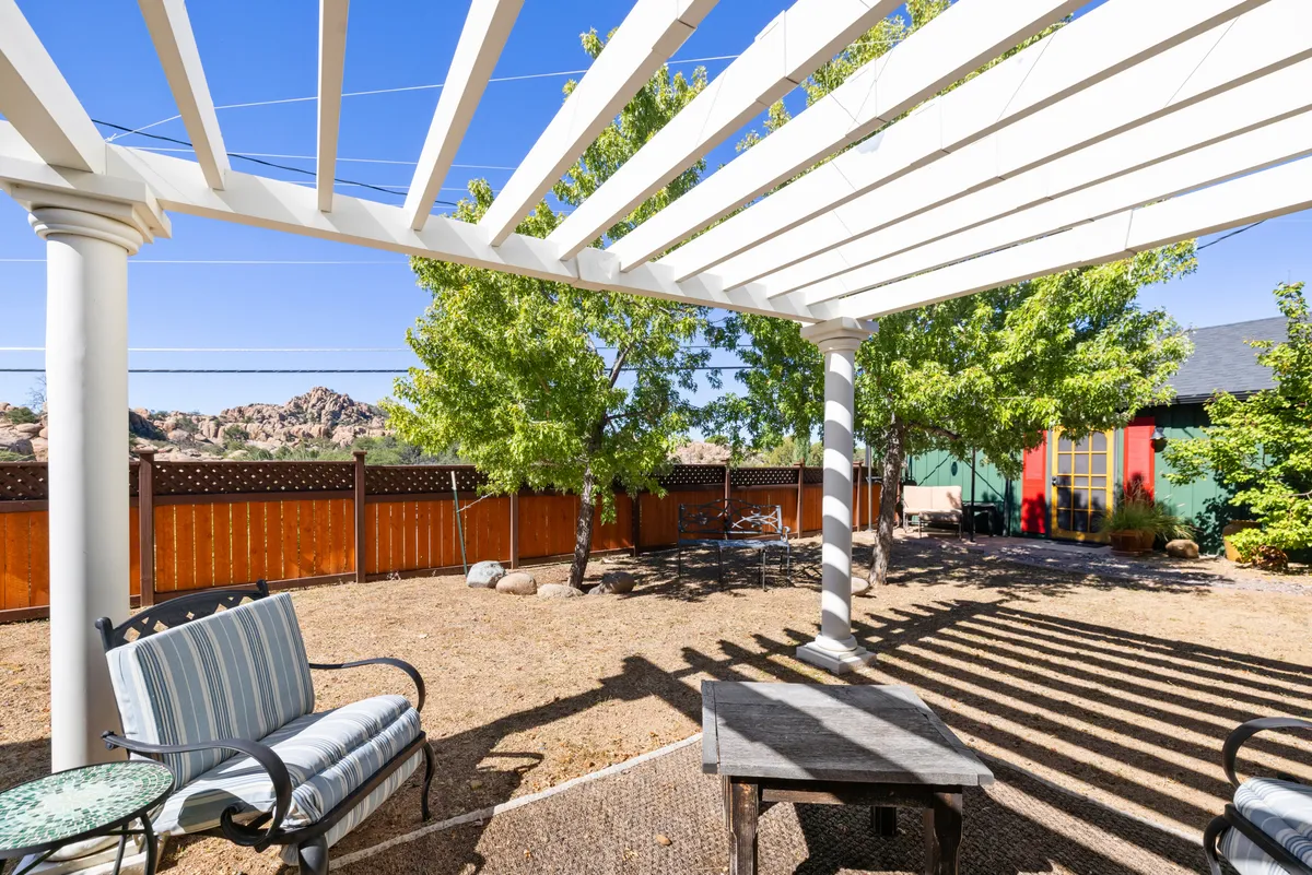 This image features a pergola structure with a comfortable seating area surrounded by lush garden greenery. In the background, impressive rocky landscapes characteristic of Prescott are visible. The tranquil setting is ideal for relaxing or socializing after a day of adventure.