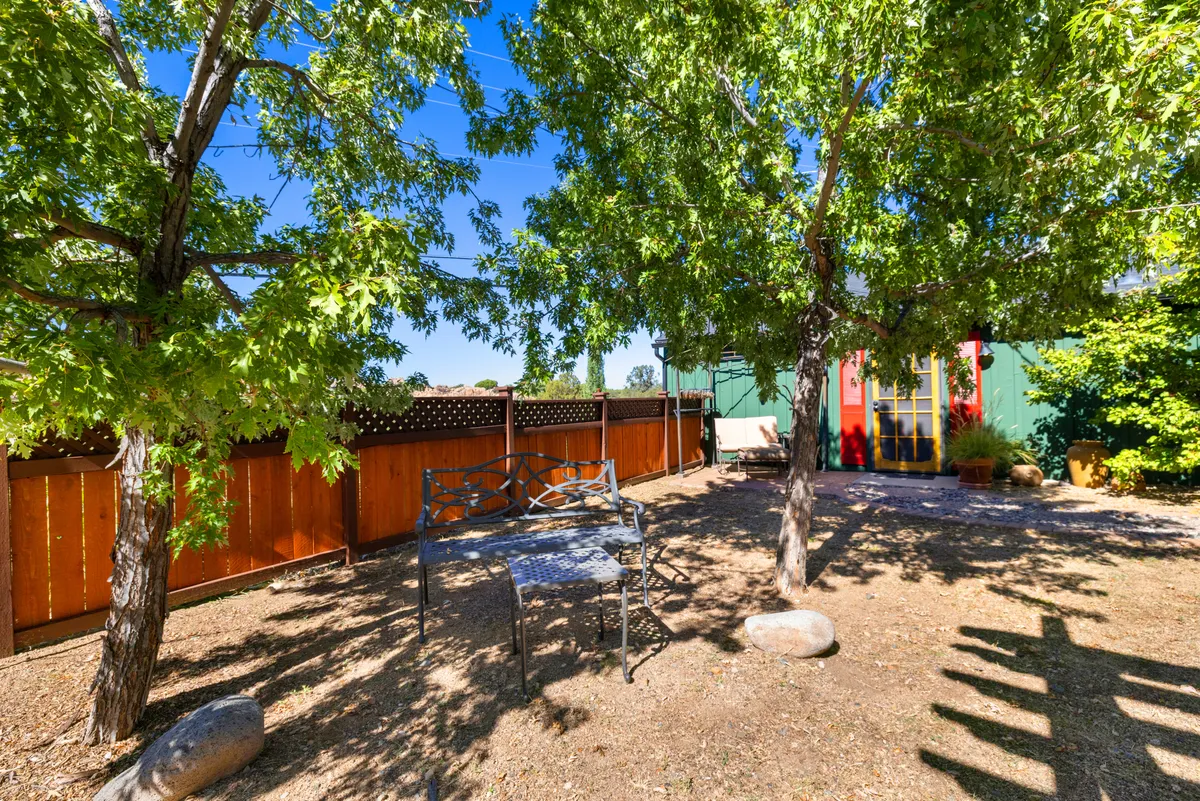The image features a metal bench set amidst green trees and a vibrantly colored door, suggesting a quiet outdoor nook. The scene radiates peace and offers a glimpse of the type of serene spots that might be found in or around historic Prescott, reinforcing the small-town atmosphere.