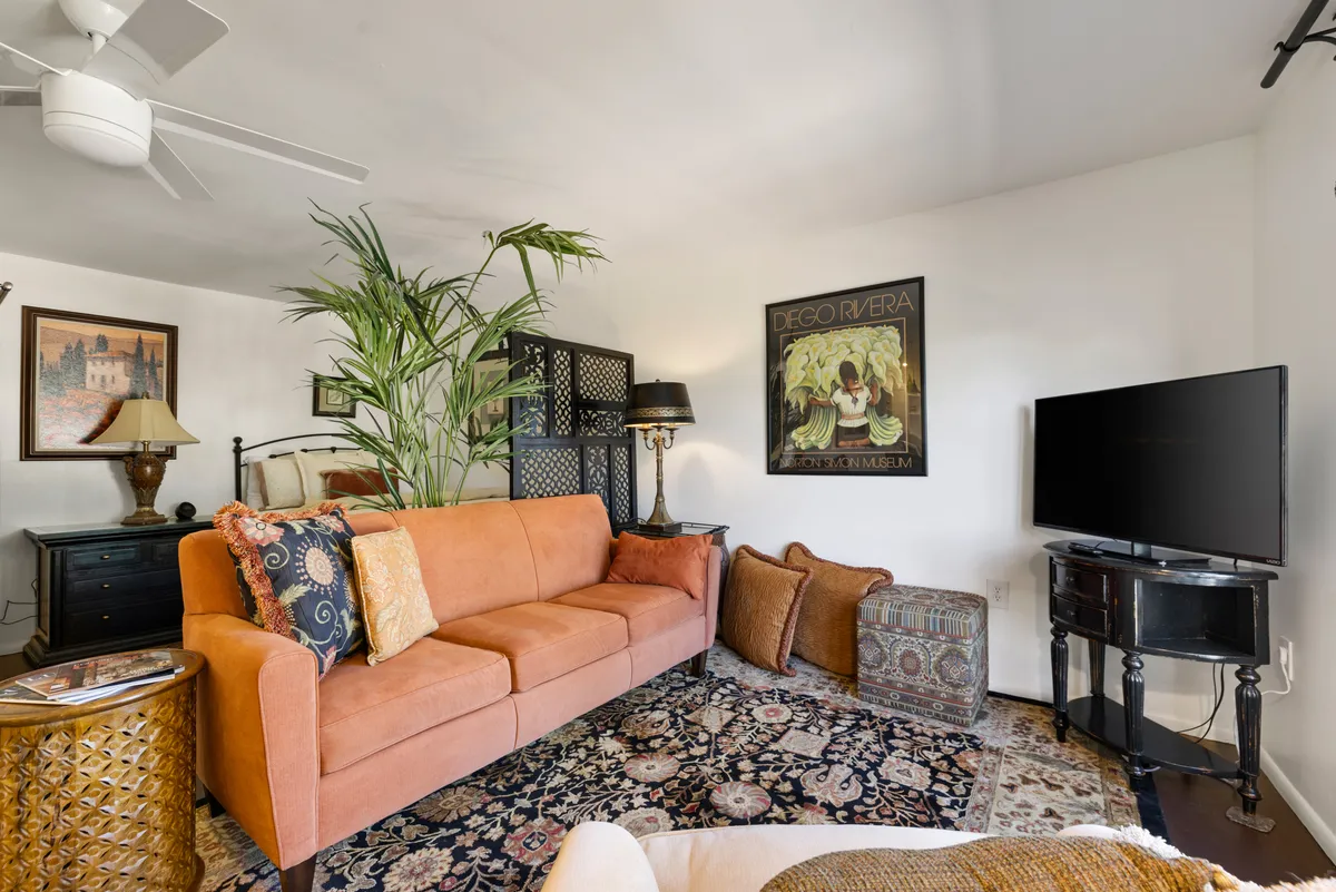 A comfortable lounge area anchored by an orange sofa, accented with decorative artwork, a leafy plant, a coffee table, and a television. The setting is both stylish and inviting, ideal for relaxed evenings and memorable conversations.