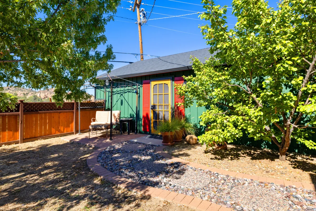 The exterior of the bungalow is shown with a vibrant, colorful door, plenty of green foliage, and a charming garden path. The scene feels welcoming, hinting at a cozy return after outdoor excursions.