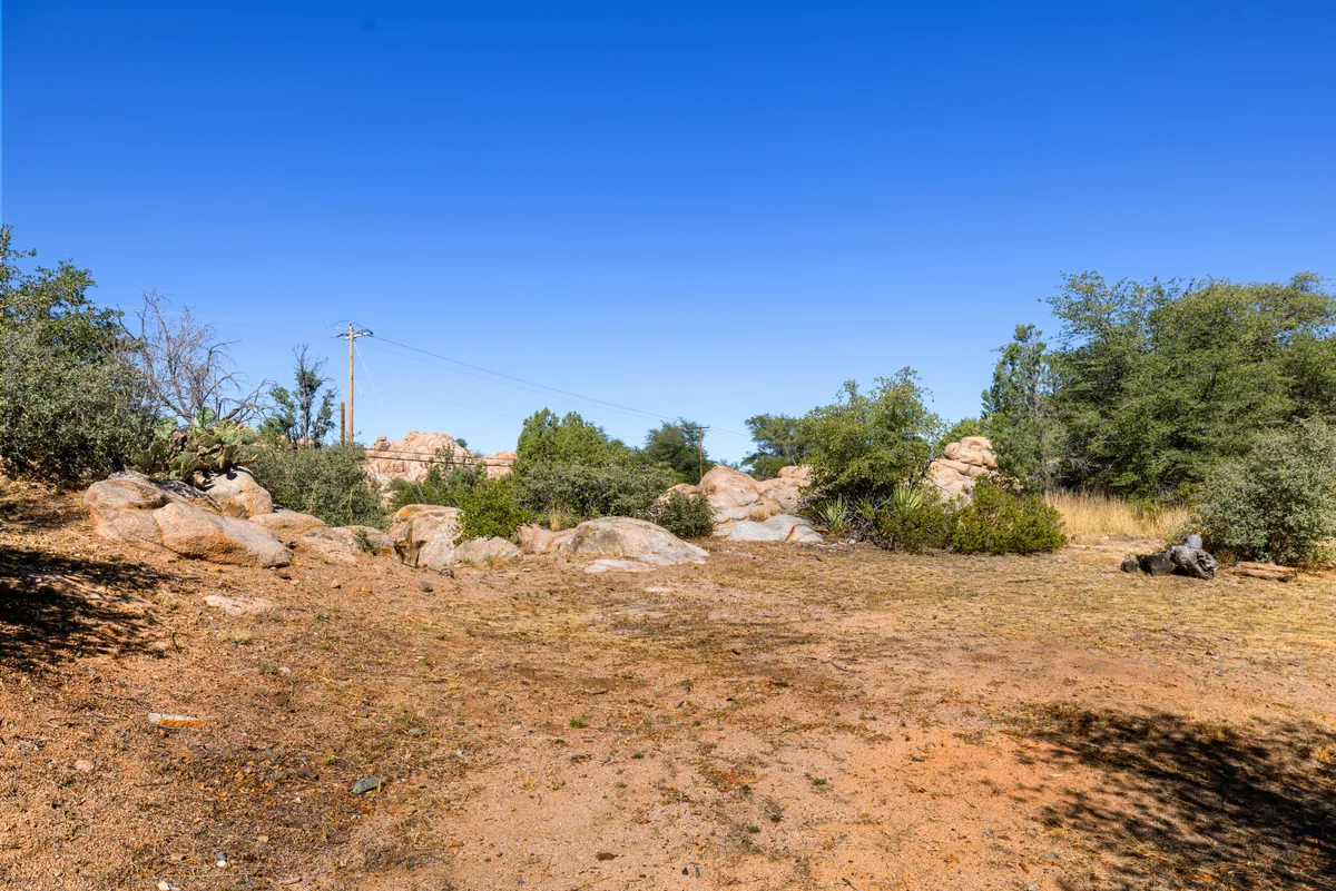 A serene exterior landscape with prominent rock formations, scattered shrubs, and distant trees. The scene evokes Prescott's unique natural setting and suggests views that could be experienced from the bedroom window.