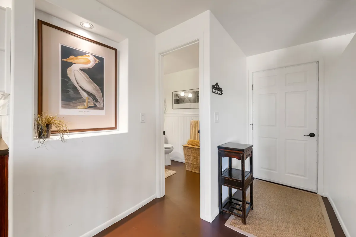 A welcoming hallway featuring a framed pelican artwork, a wooden side table, and a door leading further into the home. Soft lighting and an uncluttered surface suggest a serene transition space ideal for greeting guests or pausing after returning from outside adventures.