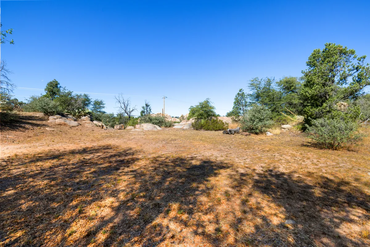 A wide view of impressive natural rock formations surrounded by scattered shrubs and open ground. The scene captures the rugged beauty of the Prescott Dells, with rocky outcrops providing dramatic visual interest and a sense of untouched nature.