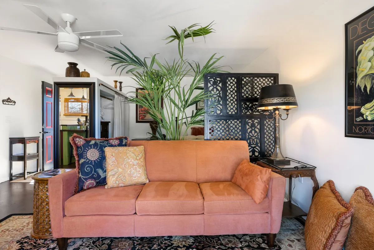 This inviting interior showcases a vibrant orange sofa accented by a lush green plant, warm decorative lighting, and tasteful artwork on the walls. The cozy space is perfect for relaxing, reading a book, or sharing warm conversations, radiating comfort and charm.