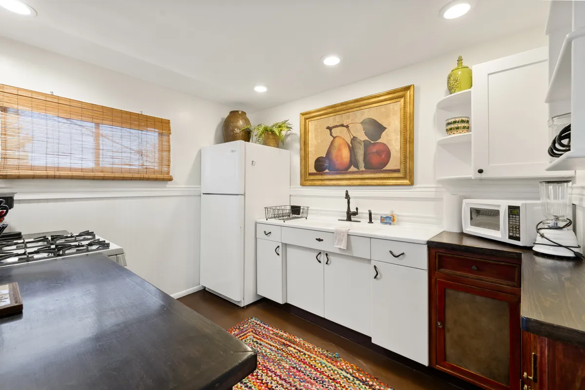 This cheerful kitchen scene features a colorful area rug, a large fruit painting, and modern appliances set against a wooden countertop. The setting radiates warmth and is clearly designed for both casual brunches and larger family gatherings.